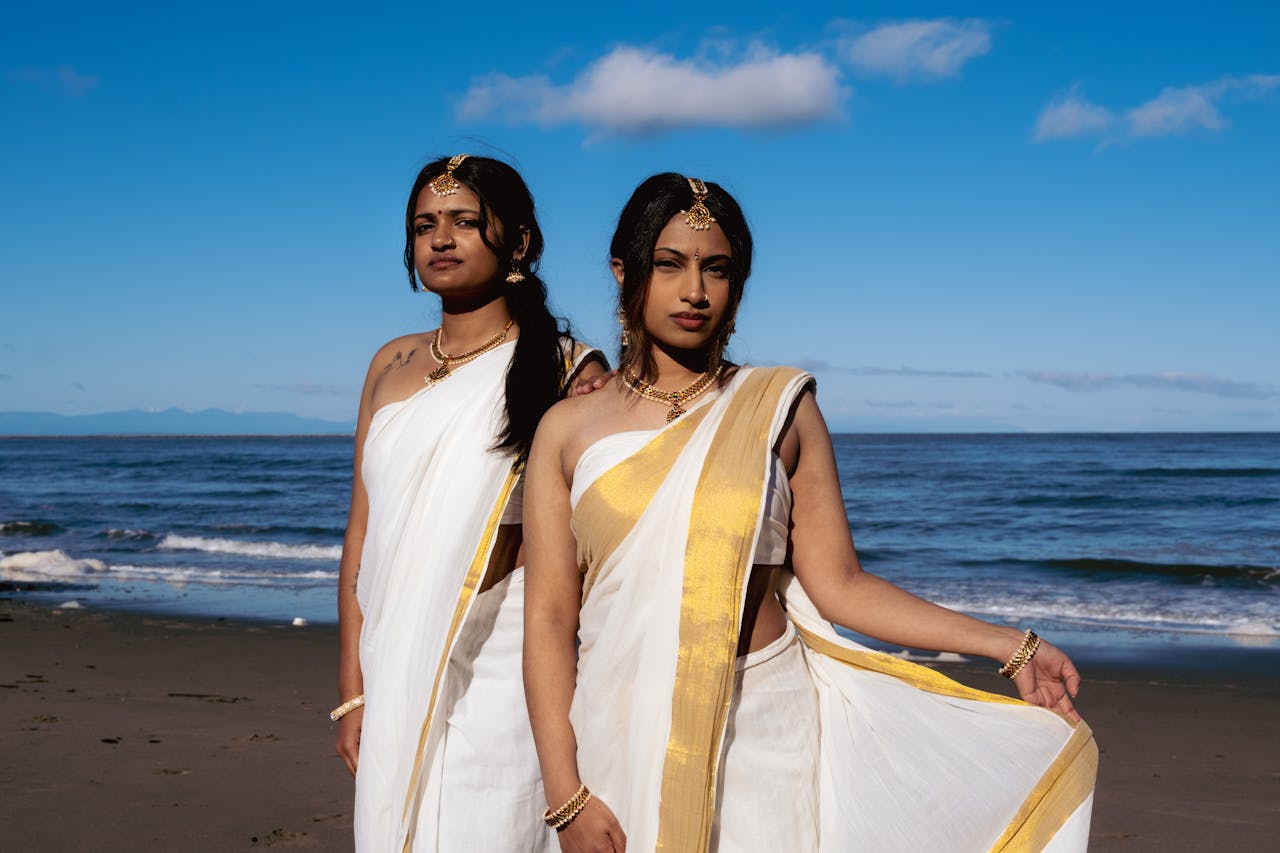 why-choose-us Two South Asian women in traditional sarees and accessories posing elegantly on a Vancouver beach during the day.