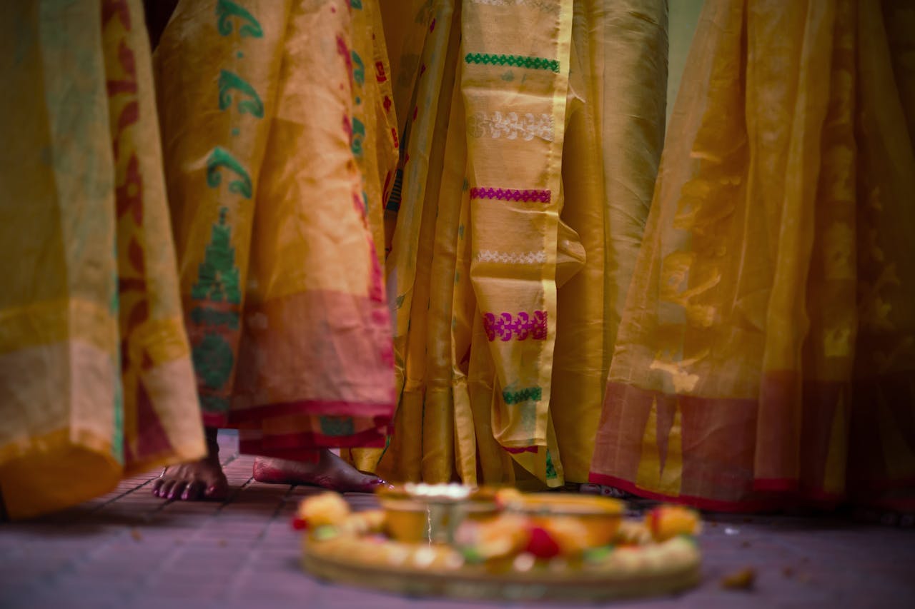 Festive scene depicting feet and sarees of women in traditional attire during a cultural ceremony.