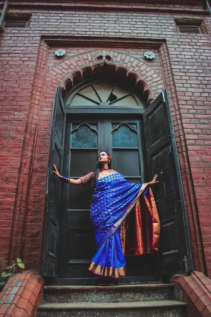 journey A woman in a vibrant saree poses dramatically in front of a historic wooden door.